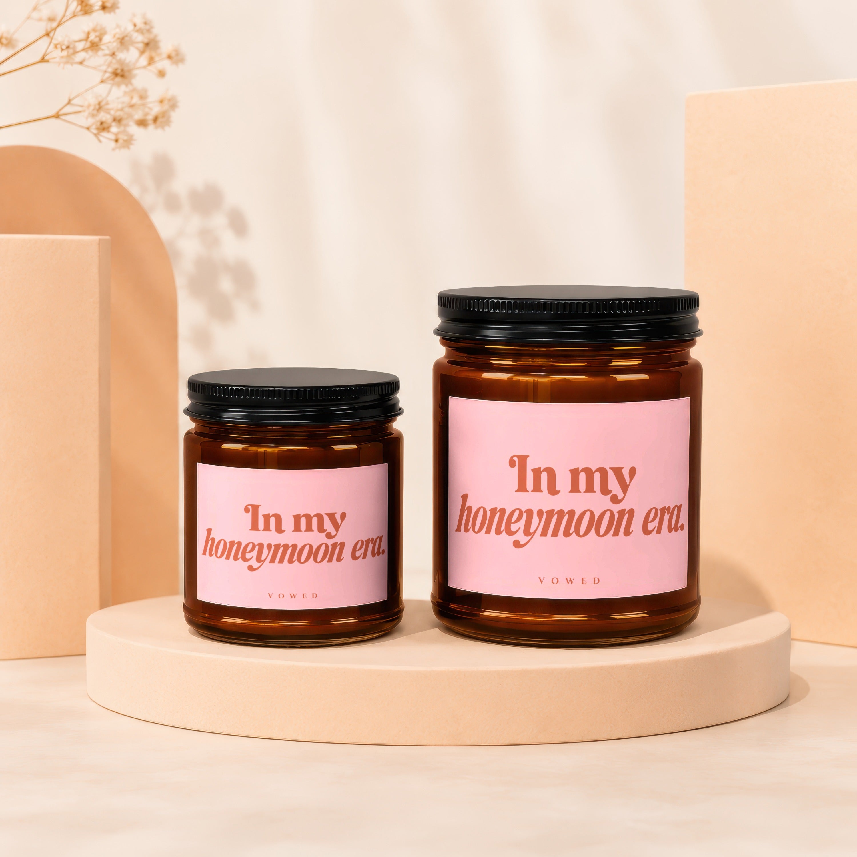 Two brown glass candles with pink labels reading "In my honeymoon era."