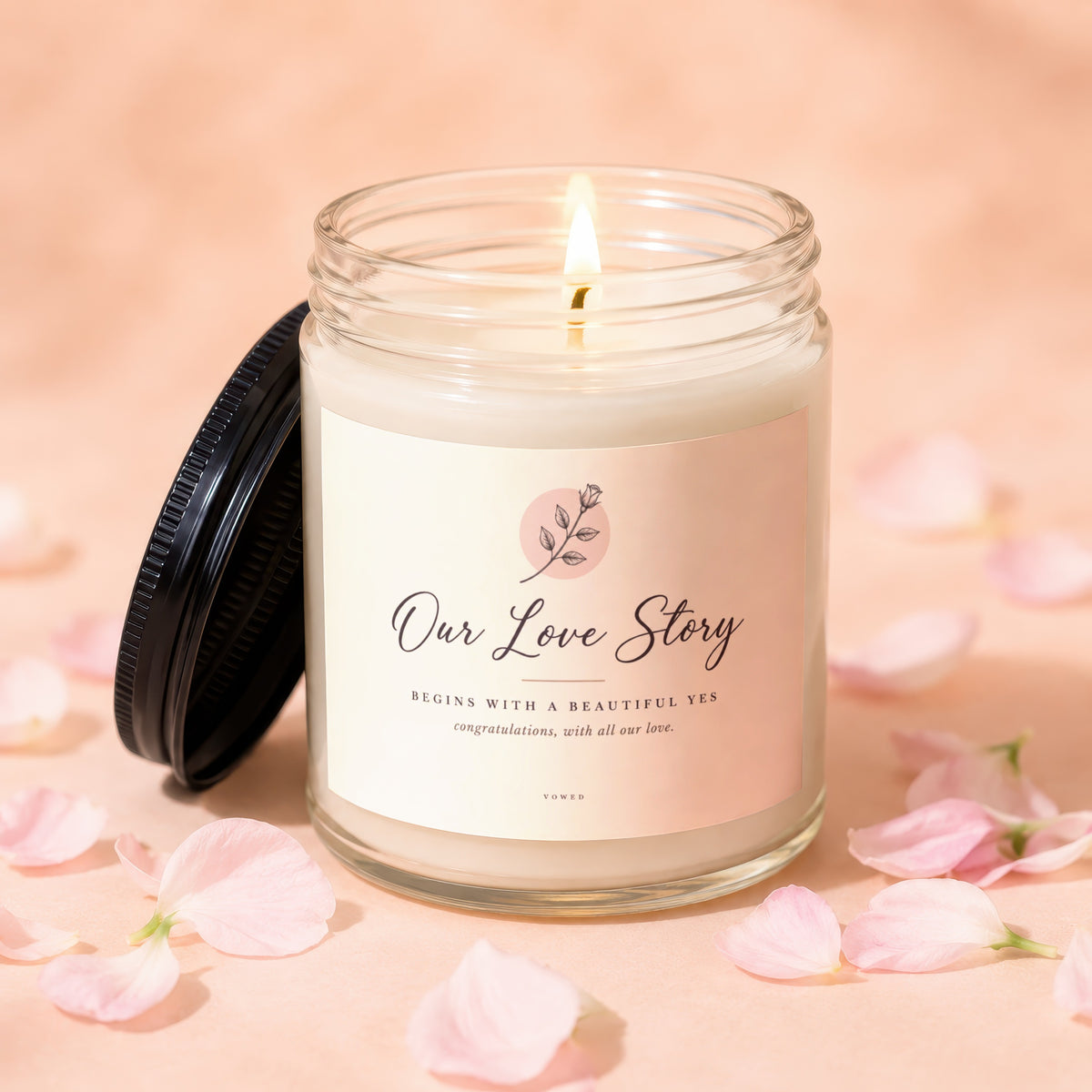 Glass candle with lit wick, "Our Love Story" text, and scattered pink petals.