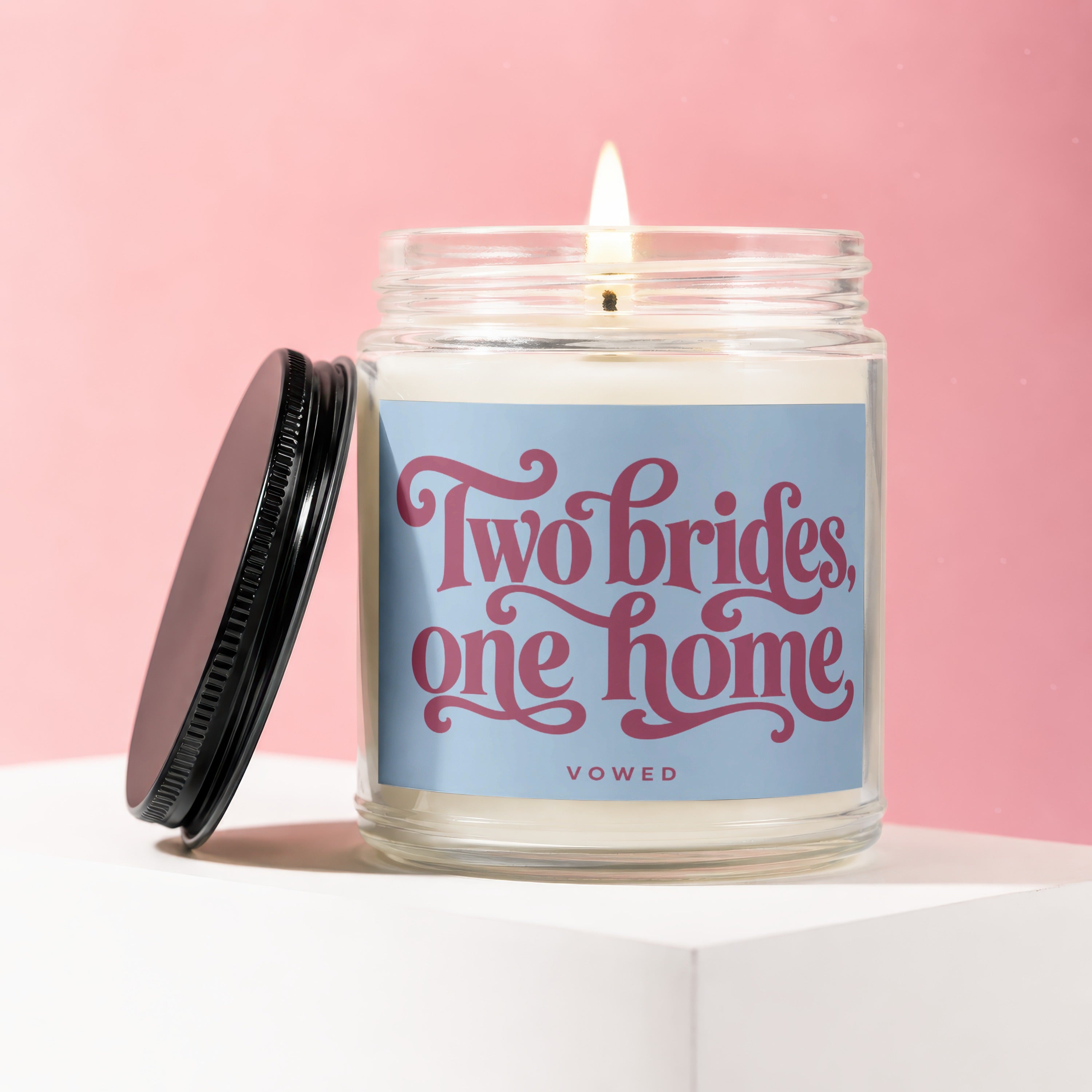 Lit candle in glass jar with lid ajar, reads "Two brides, one home"