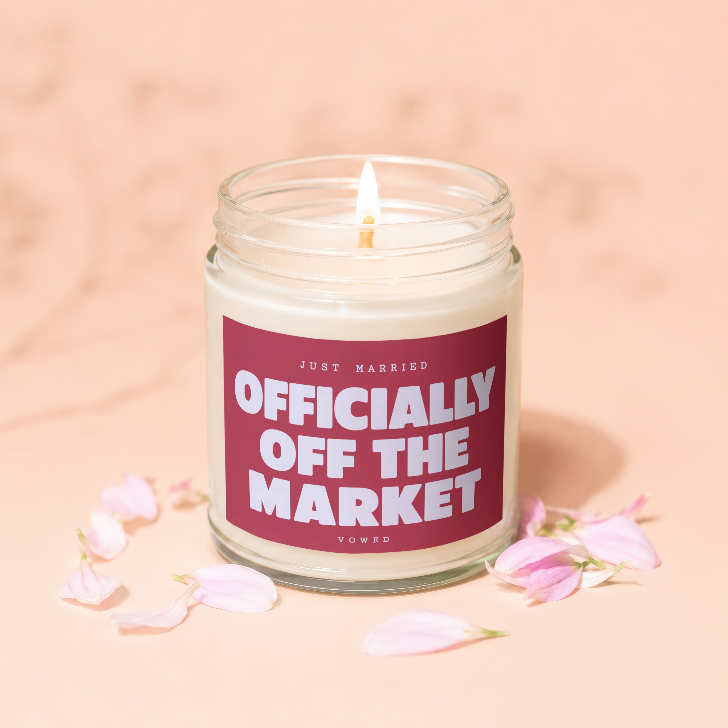 Lit candle with "Officially Off the Market" text in a jar, surrounded by flower petals.