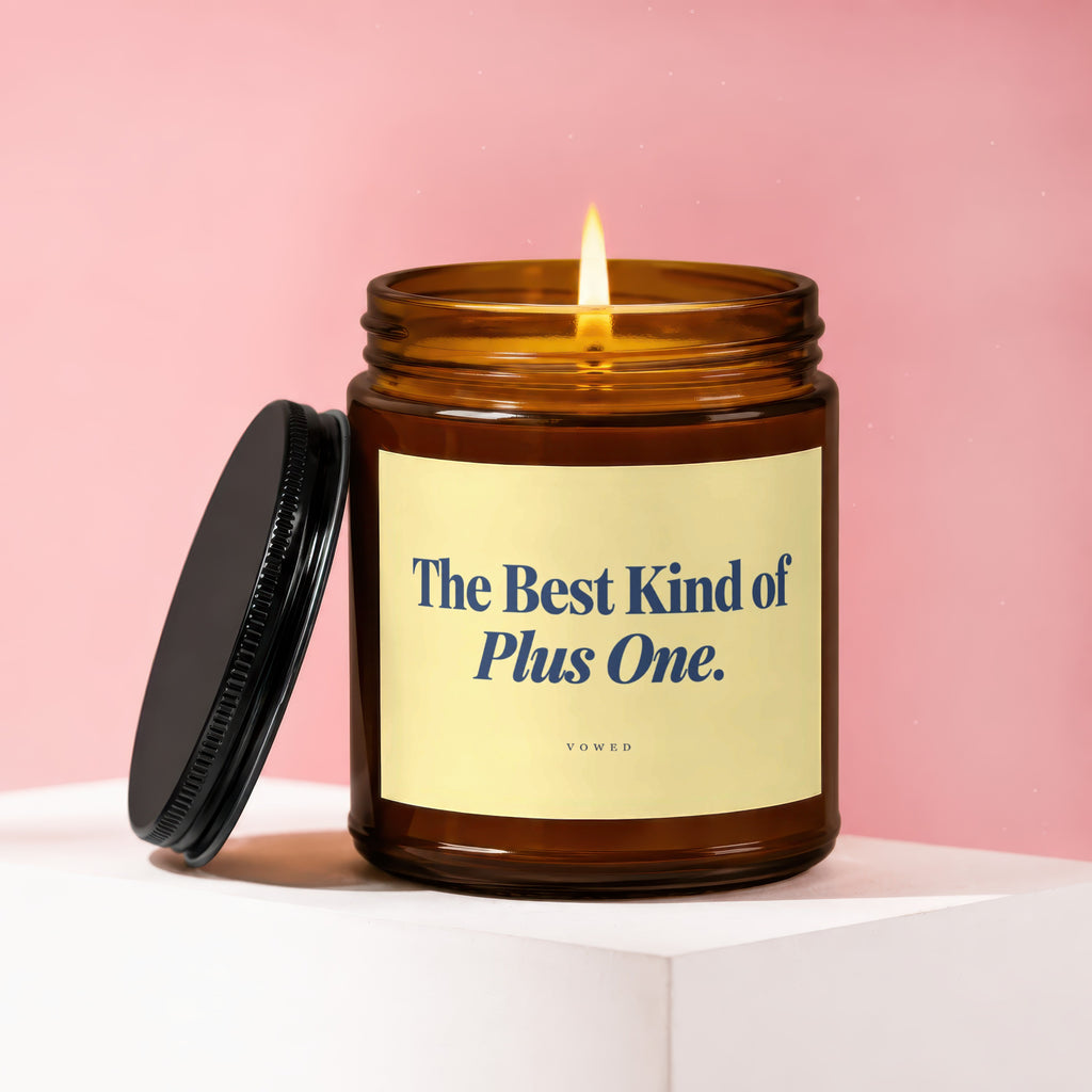 Amber candle with lit flame, black lid, and "The Best Kind of Plus One. VOWED" label.
