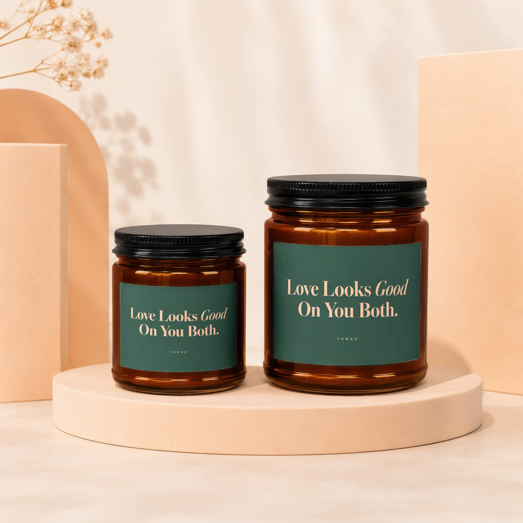 Two amber glass candles with green labels reading "Love Looks Good On You Both."