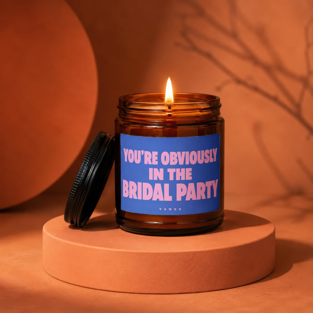 Amber glass candle with lit wick and blue label reading "YOU'RE OBVIOUSLY IN THE BRIDAL PARTY".