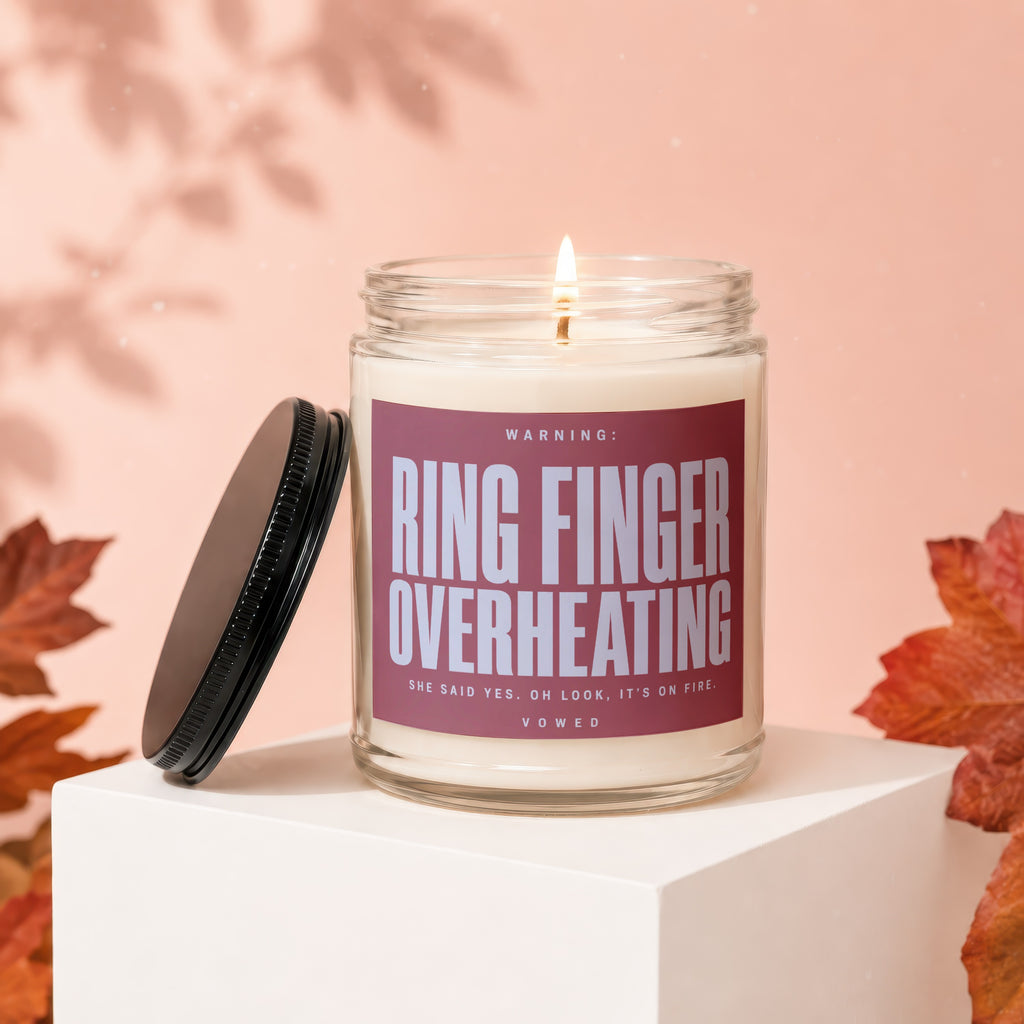 Lit candle with label "Ring Finger Overheating" on a white pedestal with autumn leaves.