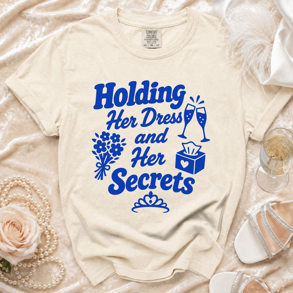 Cream t-shirt with blue text "Holding Her Dress and Her Secrets" and graphic elements.