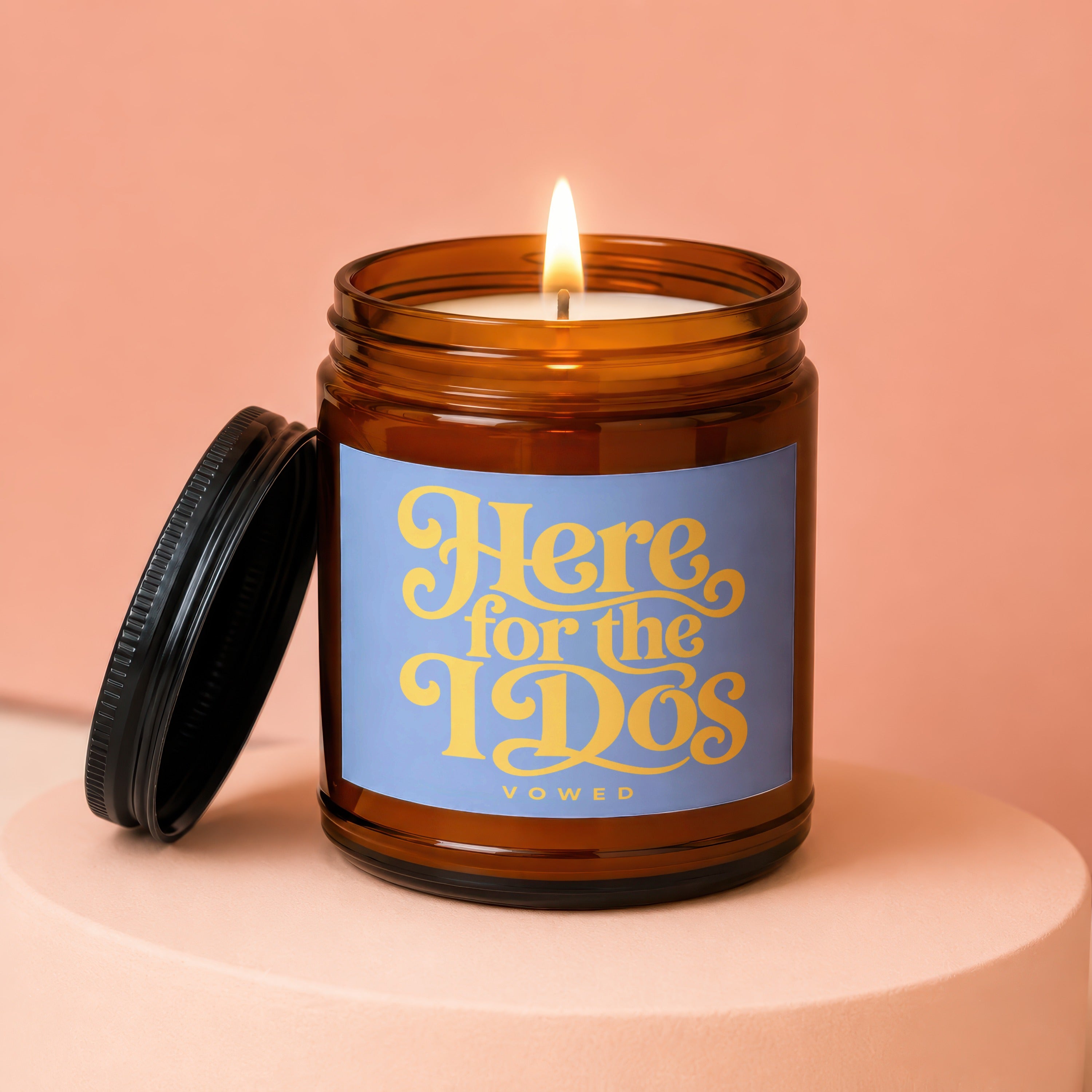 Amber jar candle with lit wick and lid off, reads "Here for the I Do's VOWED".