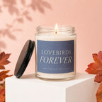 Glass jar candle with lit wick and "LOVEBIRDS FOREVER" label.