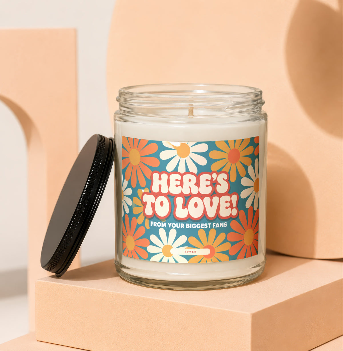 Candle with "HERE'S TO LOVE! FROM YOUR BIGGEST FANS" text and daisy pattern.