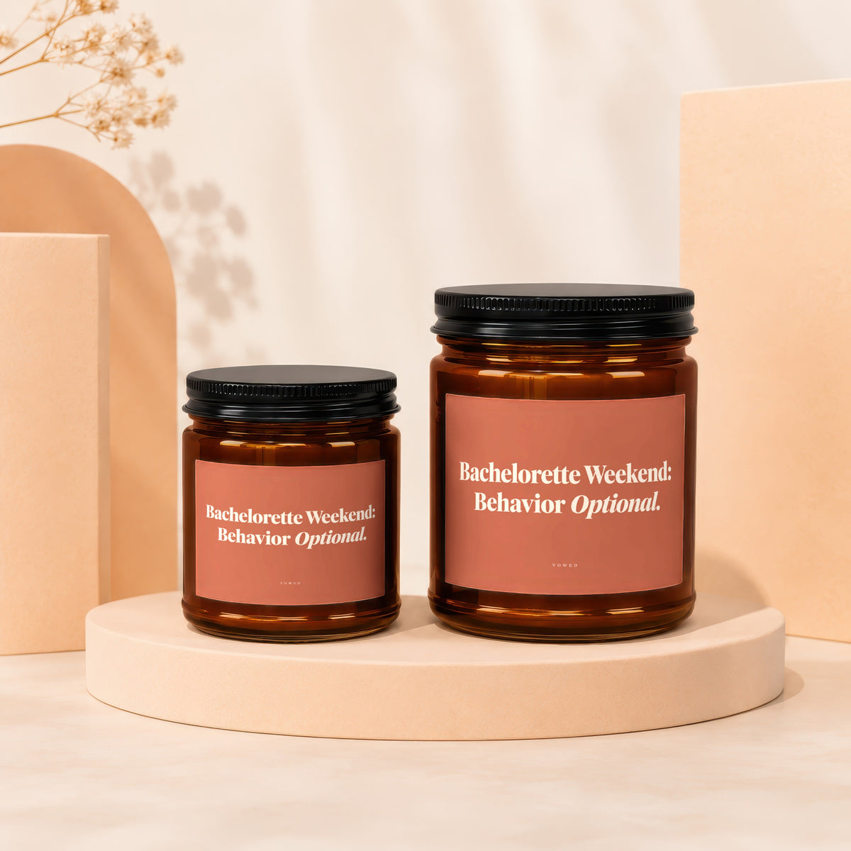 Two amber glass candles with black lids, featuring pink labels with white text.