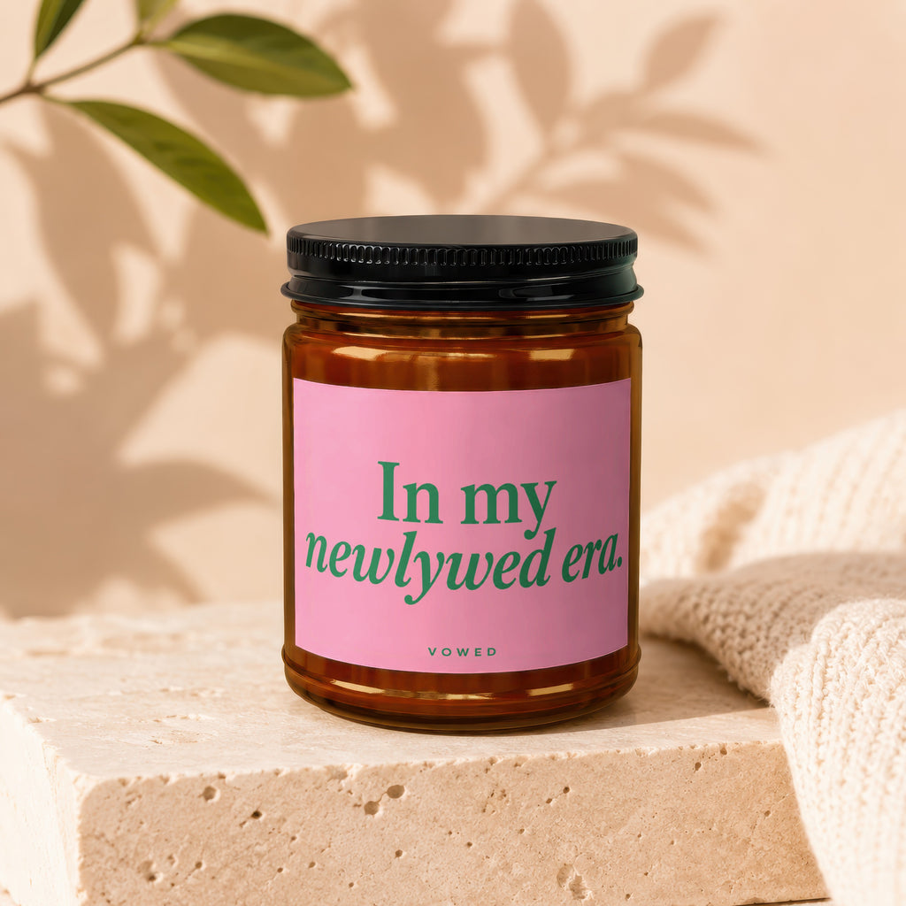 Amber candle in glass jar with pink label reading "In my newlywed era."