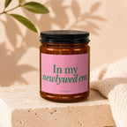Amber candle in glass jar with pink label reading "In my newlywed era."
