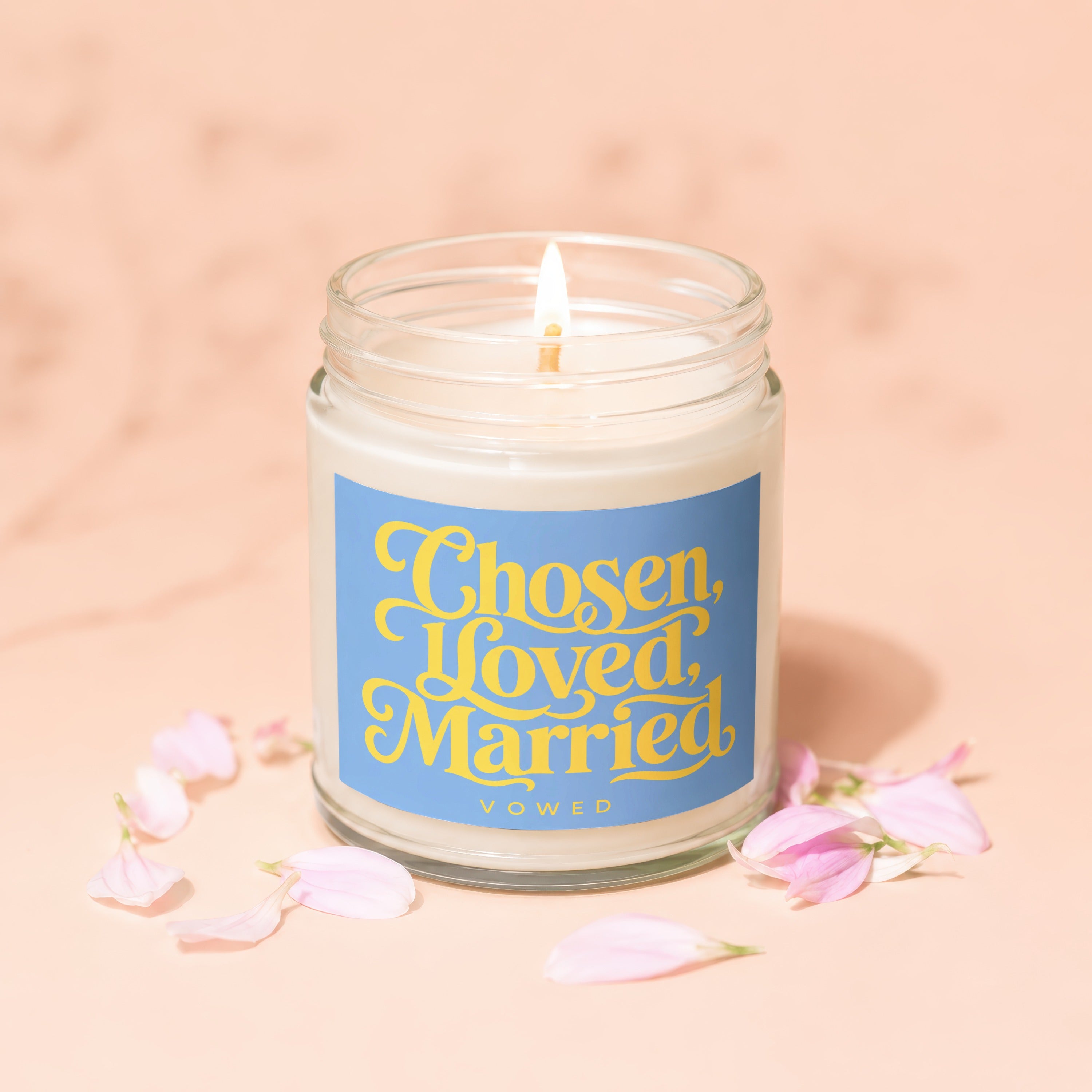 Lit candle in a glass jar with a blue label reading "Chosen, Loved, Married Vowed".