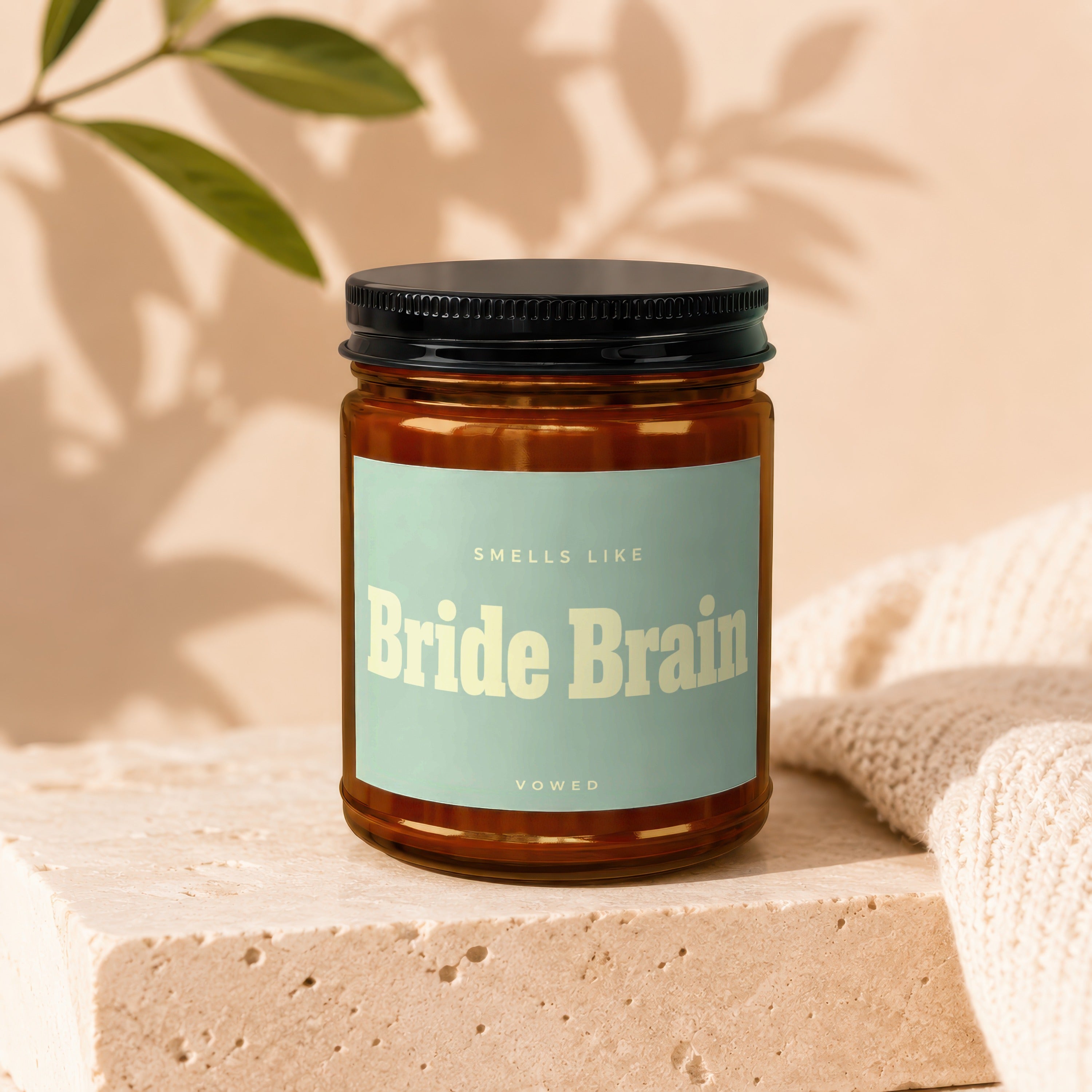 Amber jar candle labeled "Smells Like Bride Brain, Vowed" on stone pedestal.
