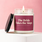 Lit candle in glass jar with burgundy label reading "The Bride Takes the Stage. Standing Ovation Expected."