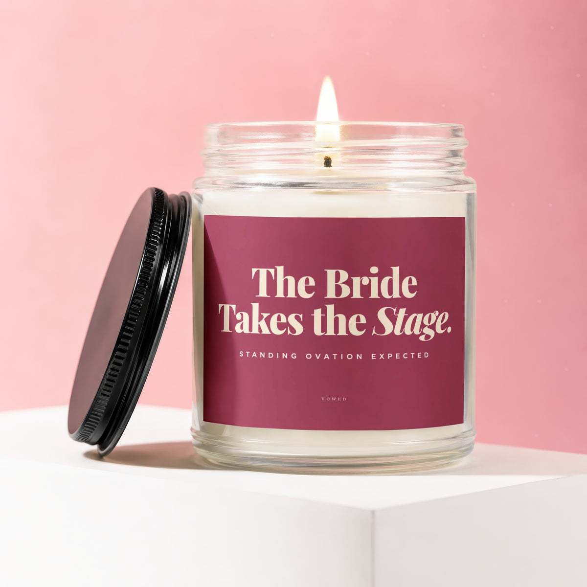 Lit candle in glass jar with burgundy label reading "The Bride Takes the Stage. Standing Ovation Expected."