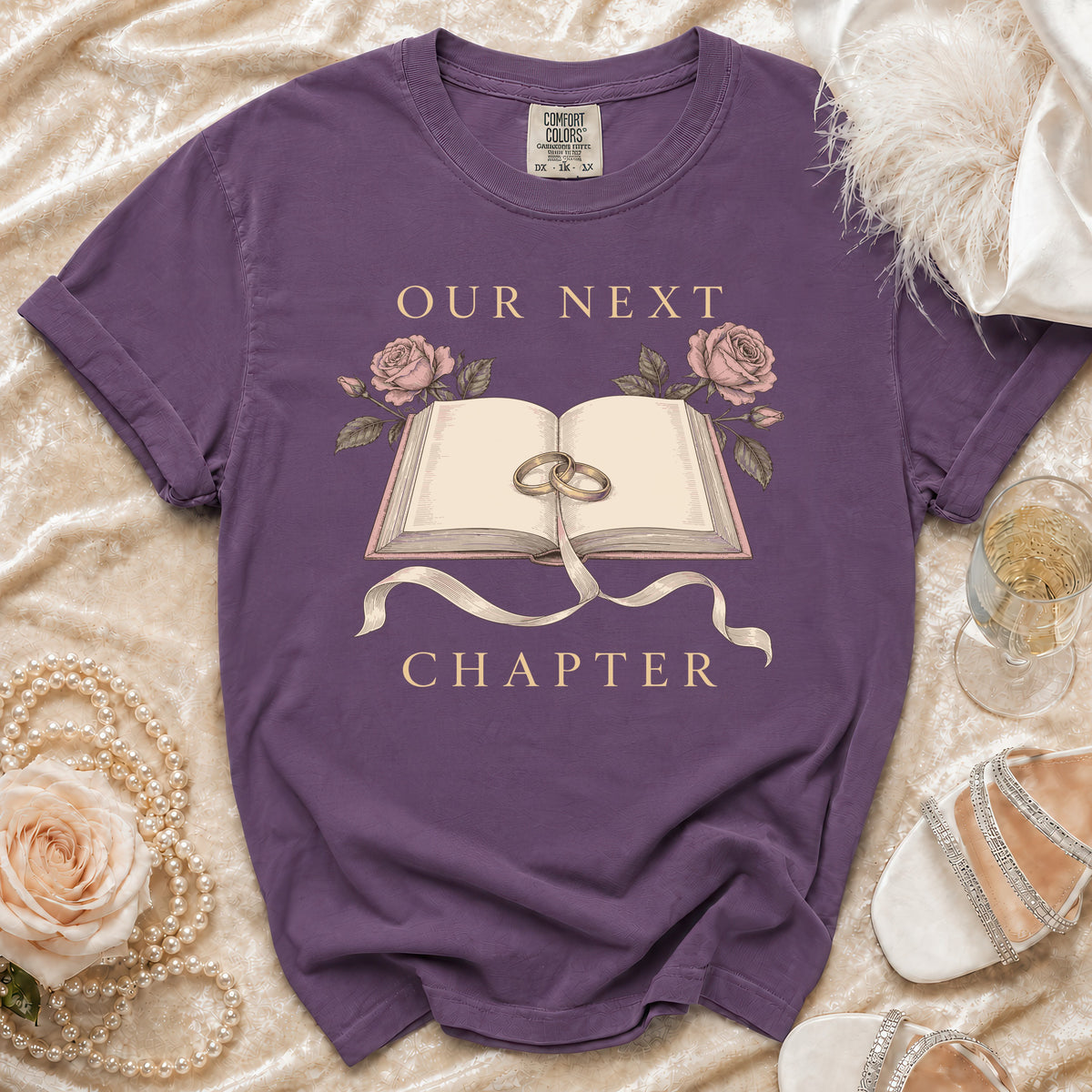 Purple t-shirt with an open book, rings, roses, and "OUR NEXT CHAPTER" text.