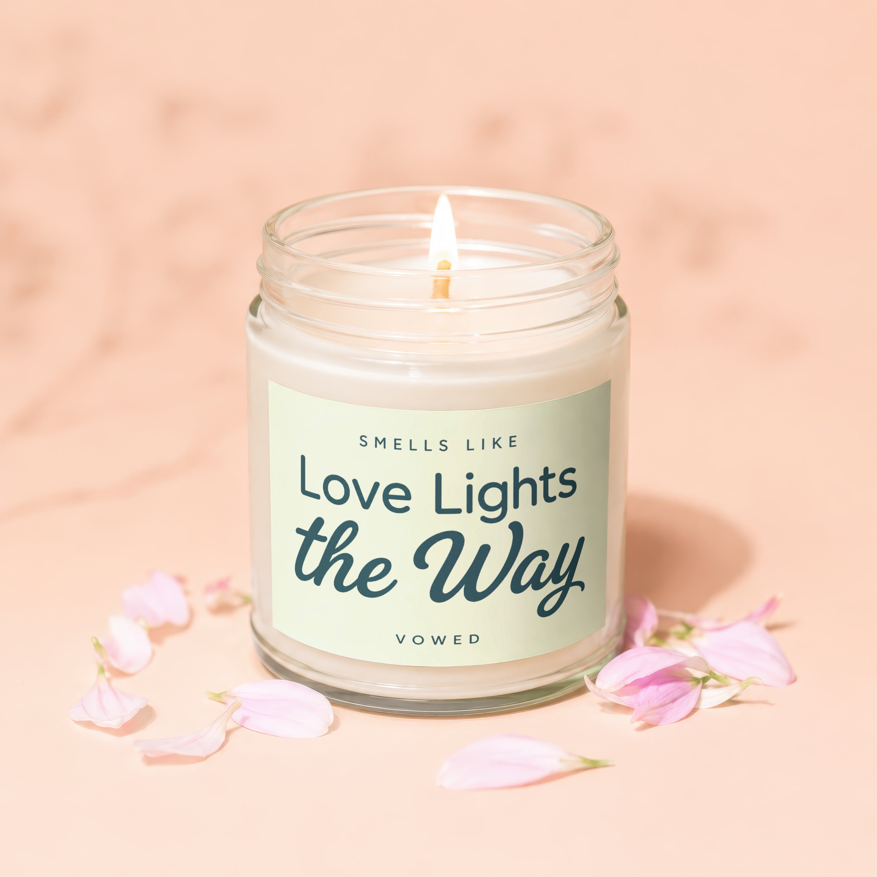 Candle with lit wick, "SMELLS LIKE Love Lights the Way VOWED" text, and pink petals.