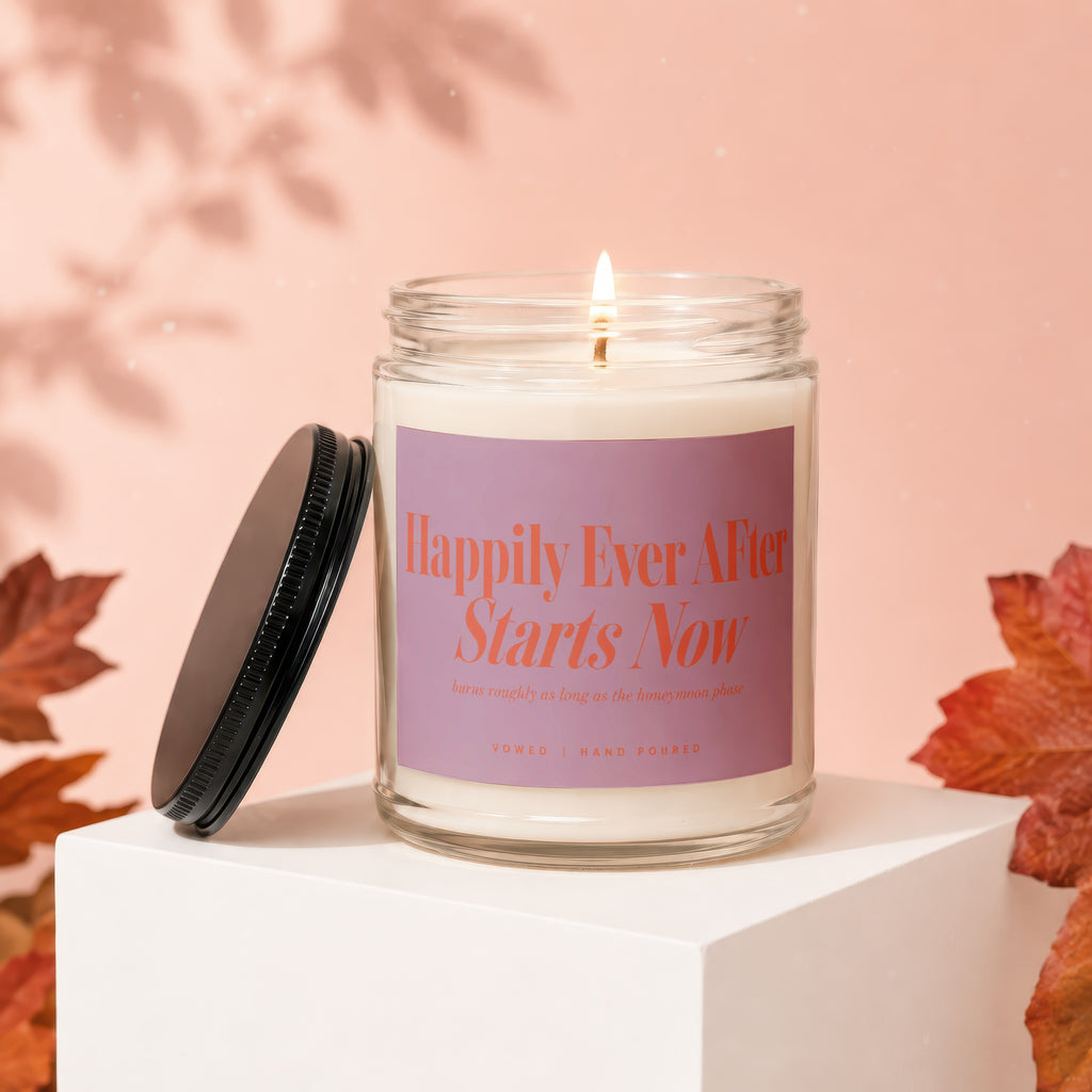 Candle with "Happily Ever After Starts Now" text, lid open, autumn leaves.