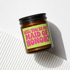 Amber jar candle with a neon green label asking "Will you be my Maid of Honor?"