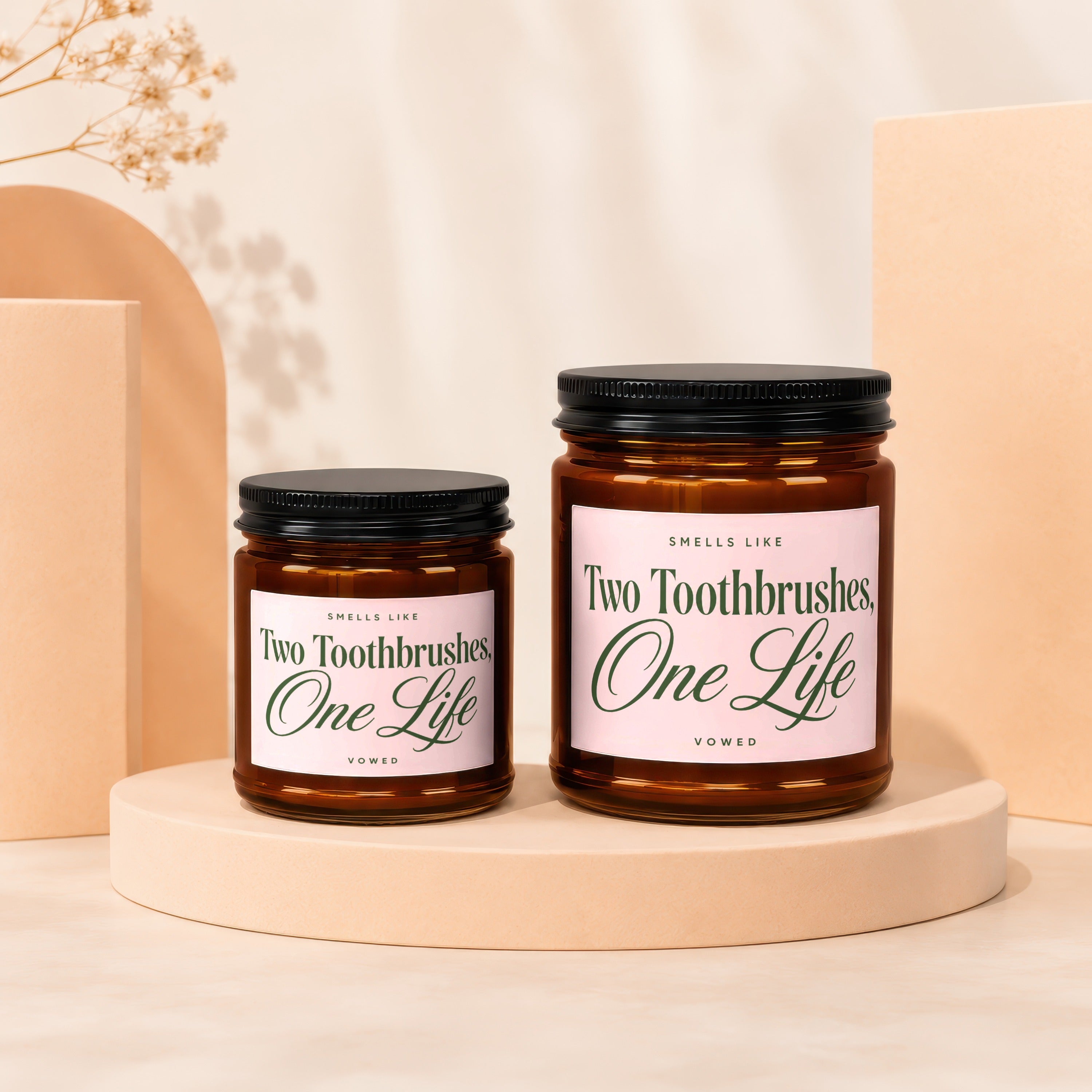 Two glass jars with black lids, featuring pink labels that say "Two Toothbrushes, One Life".