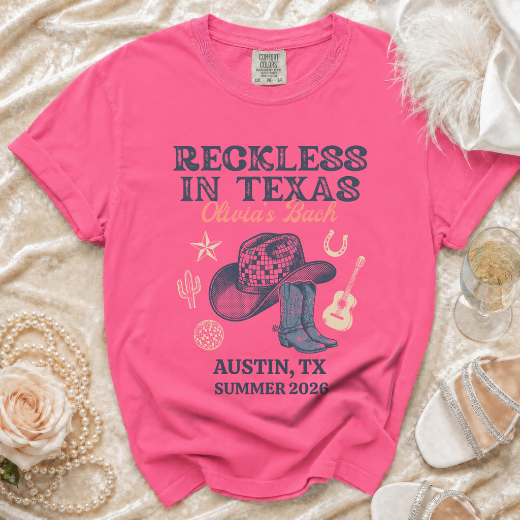 Pink t-shirt with "Reckless in Texas" and "Olivia's Bach" text, cowboy hat, boots, and guitar graphic.