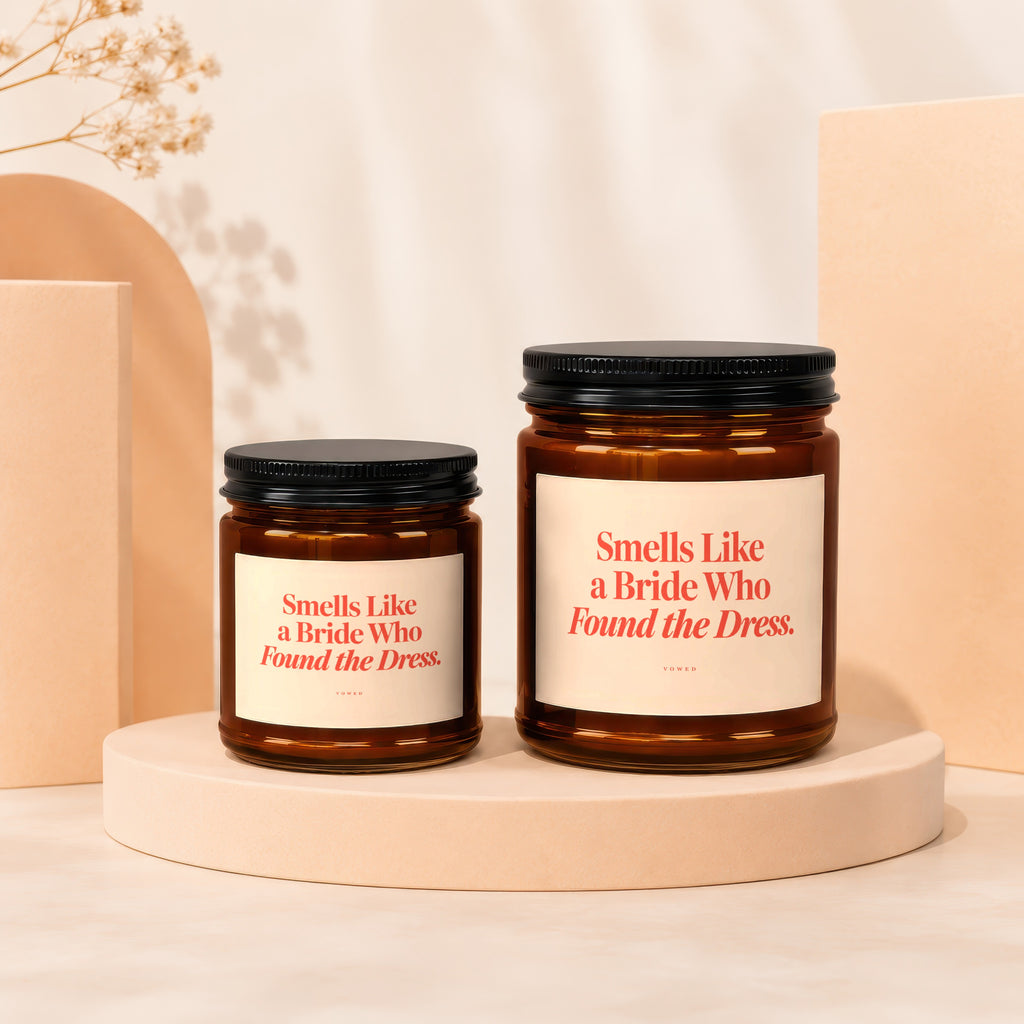 Two amber glass candles with black lids and labels reading "Smells Like a Bride Who Found the Dress."