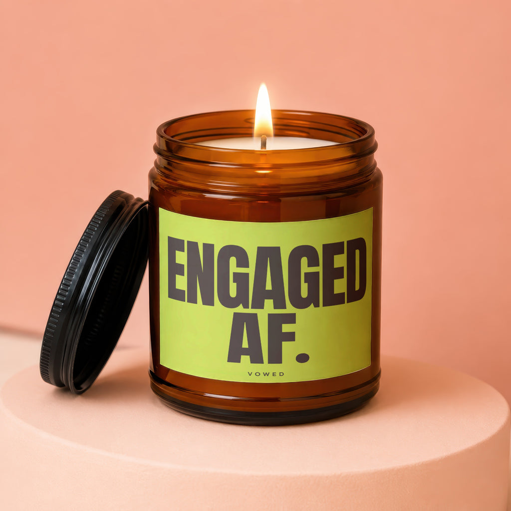 Lit candle in amber jar with "ENGAGED AF. VOWED" on lime green label.