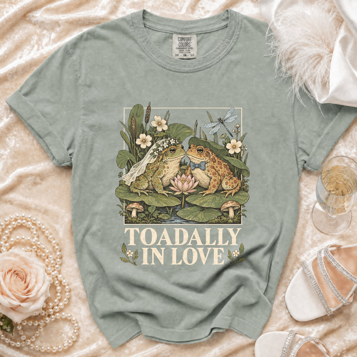 T-shirt with illustration of two frogs, one in a veil and the other in a bow tie, and text "TOADALLY IN LOVE".