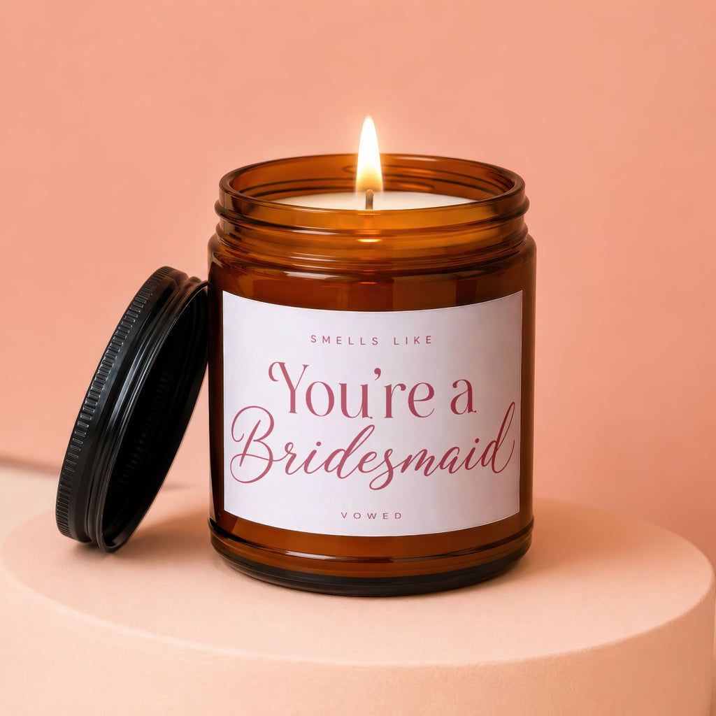 Amber jar candle lit with a label reading "Smells like You're a Bridesmaid Vowed".