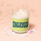 Candle with "ENGAYGED" text and pink flower petals on a peach surface.