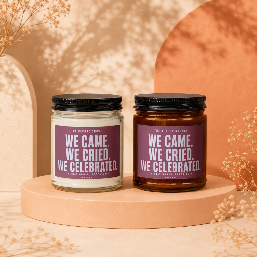 Two candles, one white and one amber, with labels reading "WE CAME. WE CRIED. WE CELEBRATED."