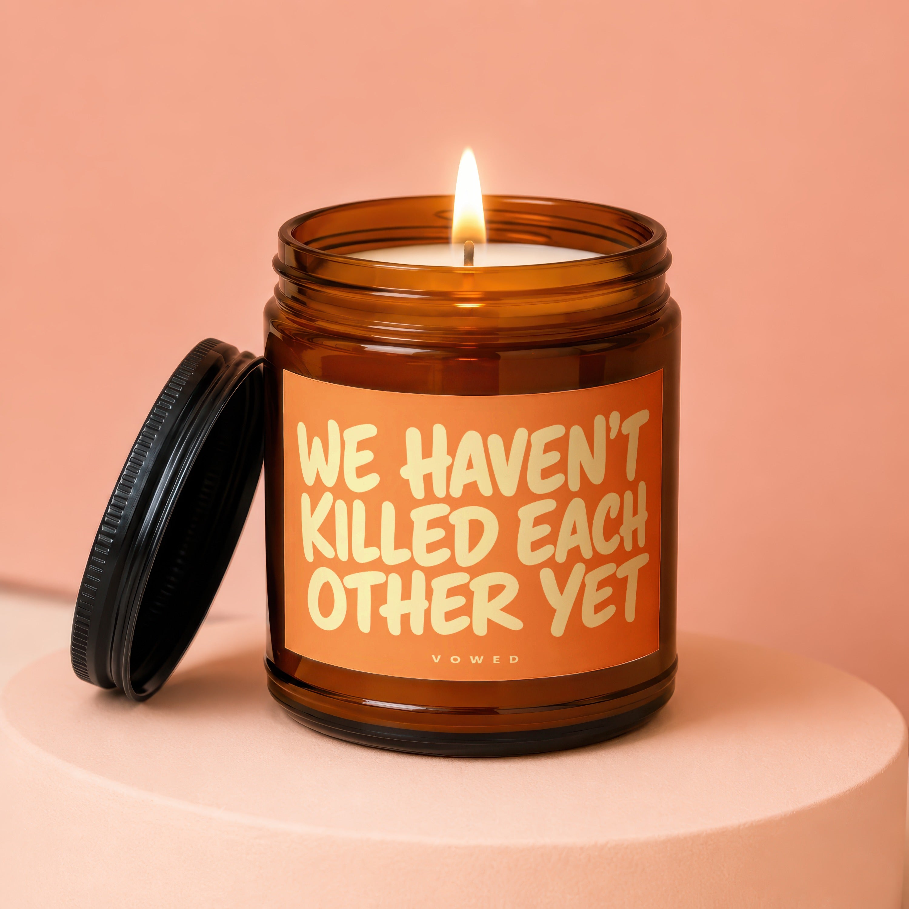 Amber jar candle with lit flame and text "WE HAVEN'T KILLED EACH OTHER YET."