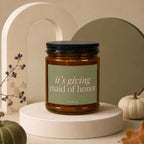 Amber candle with black lid and green label reading "it's giving maid of honor".