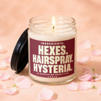 Jar candle with lit wick, dark lid, and label reading "INGREDIENTS: HEXES. HAIRSPRAY. HYSTERIA."