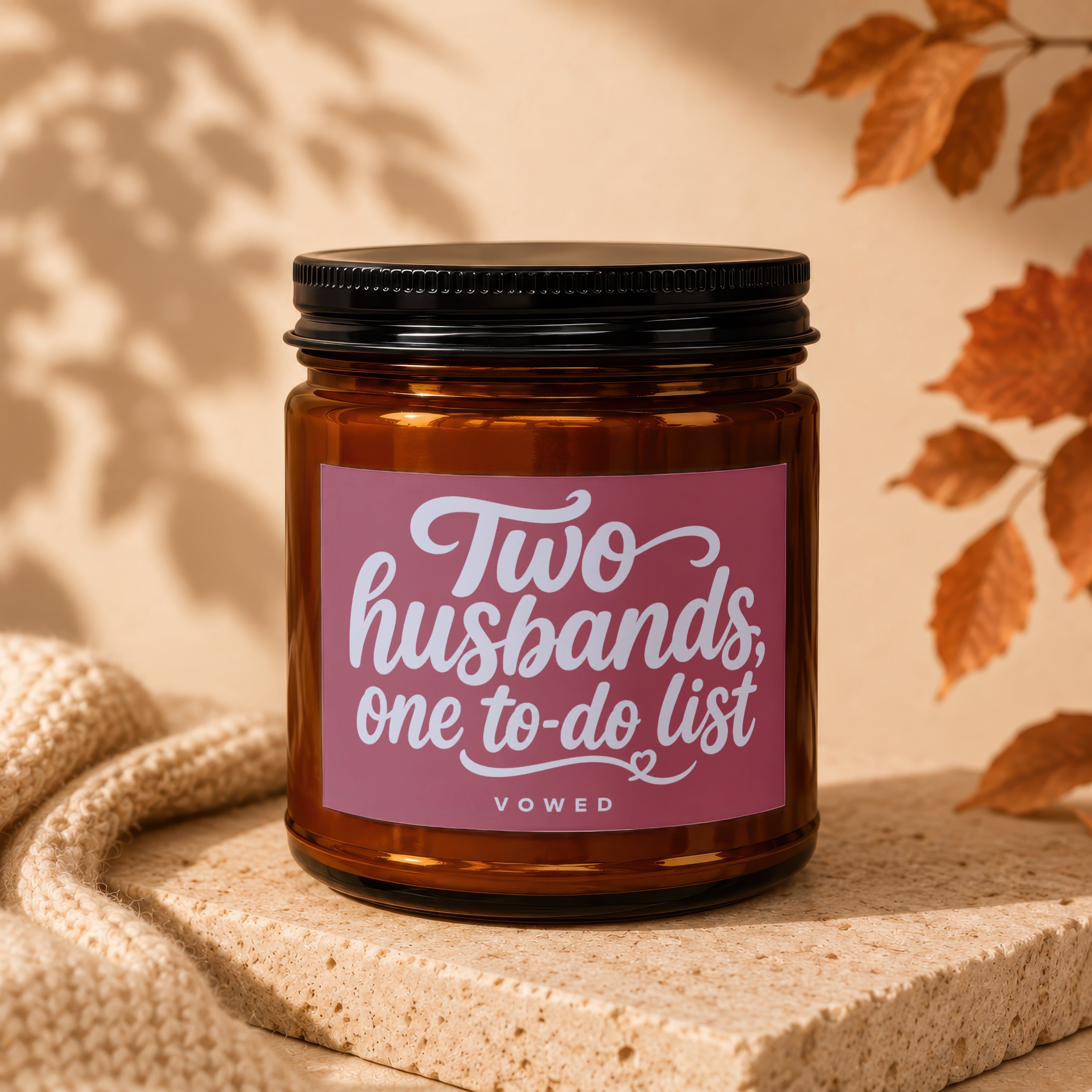 Brown glass candle with pink label reading "Two husbands, one to-do list".