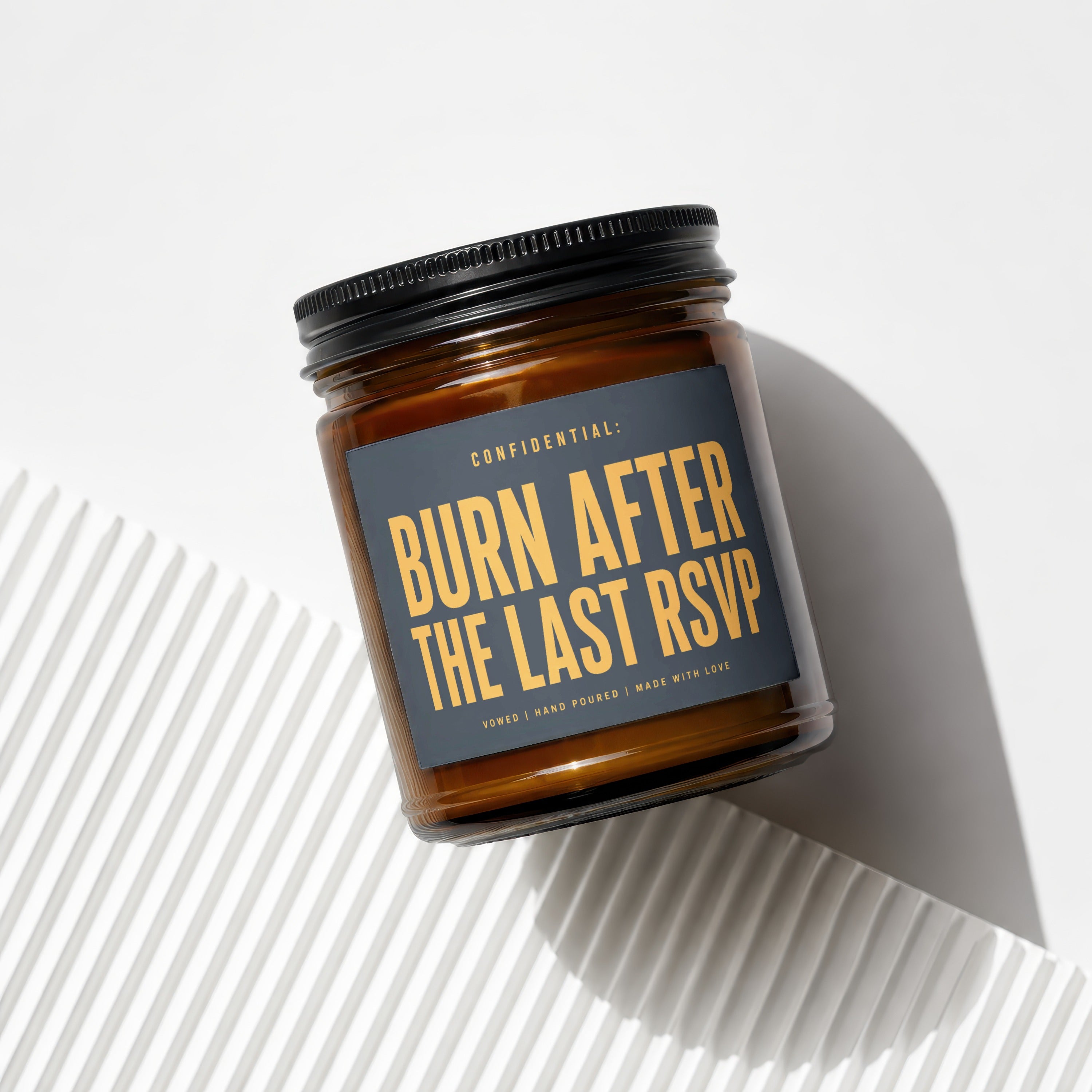 Amber jar candle with dark gray label that reads "CONFIDENTIAL: BURN AFTER THE LAST RSVP".