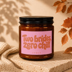 Amber jar candle with pink label reading "Two brides, zero chill."