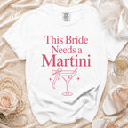 White t-shirt with pink text "This Bride Needs a Martini" and martini glass graphic.