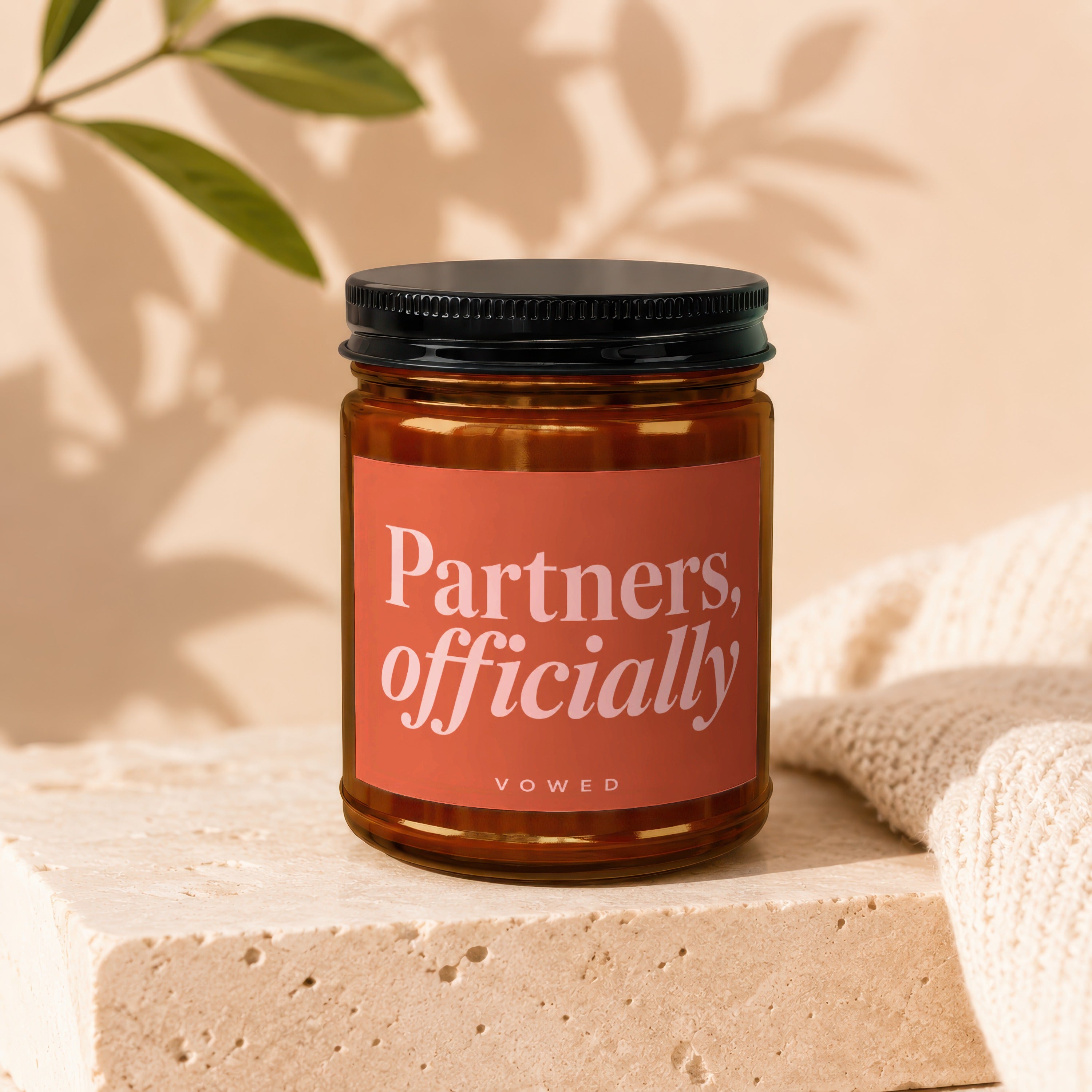 Amber glass candle with "Partners, officially VOWED" label on a cream textured surface.