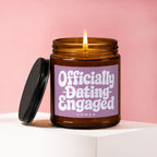 Lit amber glass candle with pink label reading "Officially Dating Engaged VOWED".