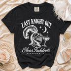Black Comfort Colors t-shirt featuring white text that reads Last Knight Out above a plumed knight helmet, a champagne glass, a crescent moon, and the text Olivia's Bachelorette Savannah, GA.