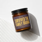 Amber jar candle with black lid reading "Survived the family drama."