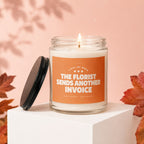 Lit candle with orange label reading "THE FLORIST SENDS ANOTHER INVOICE".