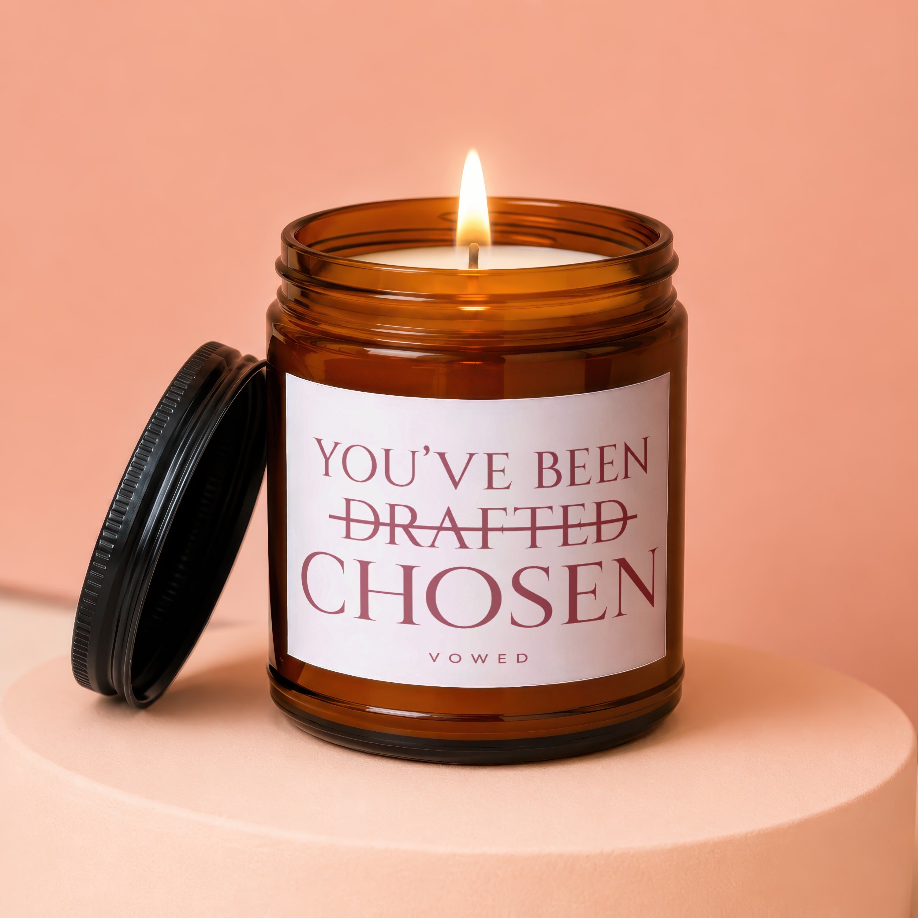 Amber jar candle with lit wick reading "You've been chosen" with "drafted" crossed out.