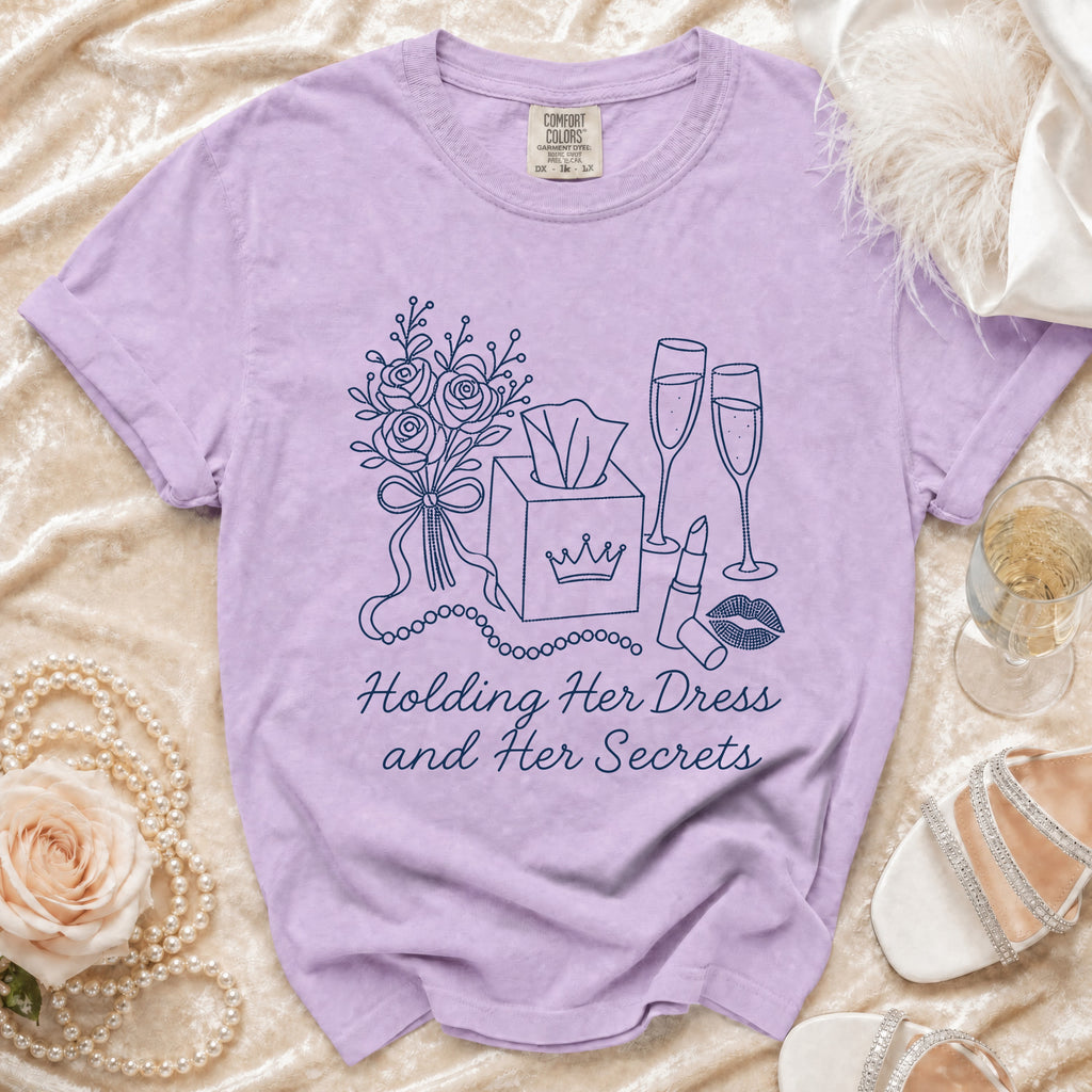 Lavender t-shirt with illustrations of roses, tissues, champagne, lipstick, and the text "Holding Her Dress and Her Secrets".