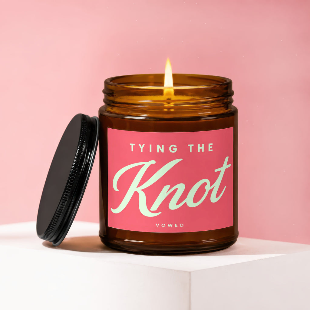Amber candle with "Tying The Knot Vowed" on pink label, lid off.