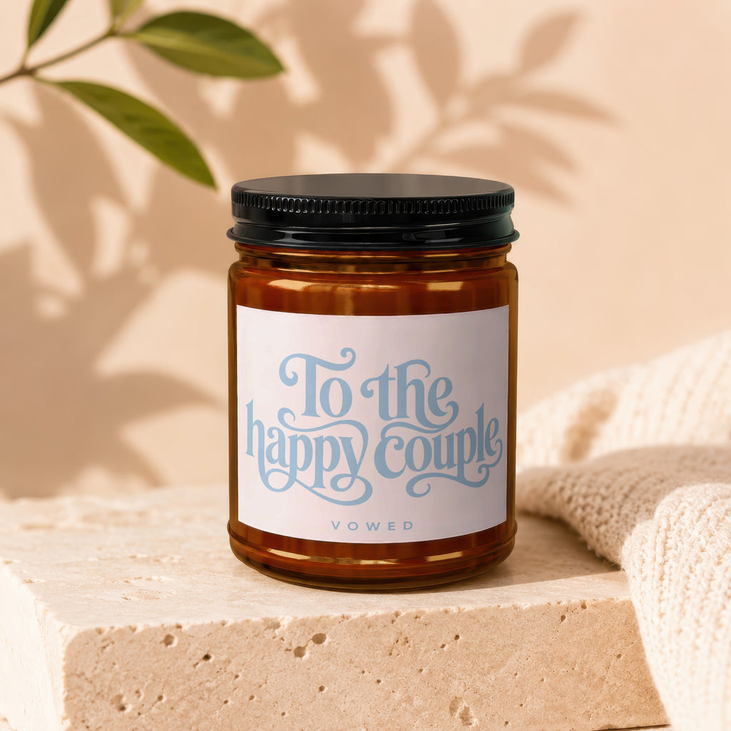 Amber jar candle with label reading "To the happy couple VOWED" on a stone block.