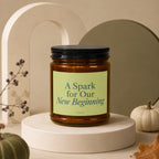 Amber candle with black lid, reads "A Spark for Our New Beginning" Vowed.