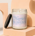 Candle with "Married the plot twist" text and black lid on display blocks.
