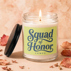 Candle with "Squad of Honor VOWED" text and a lit wick on a peach background.